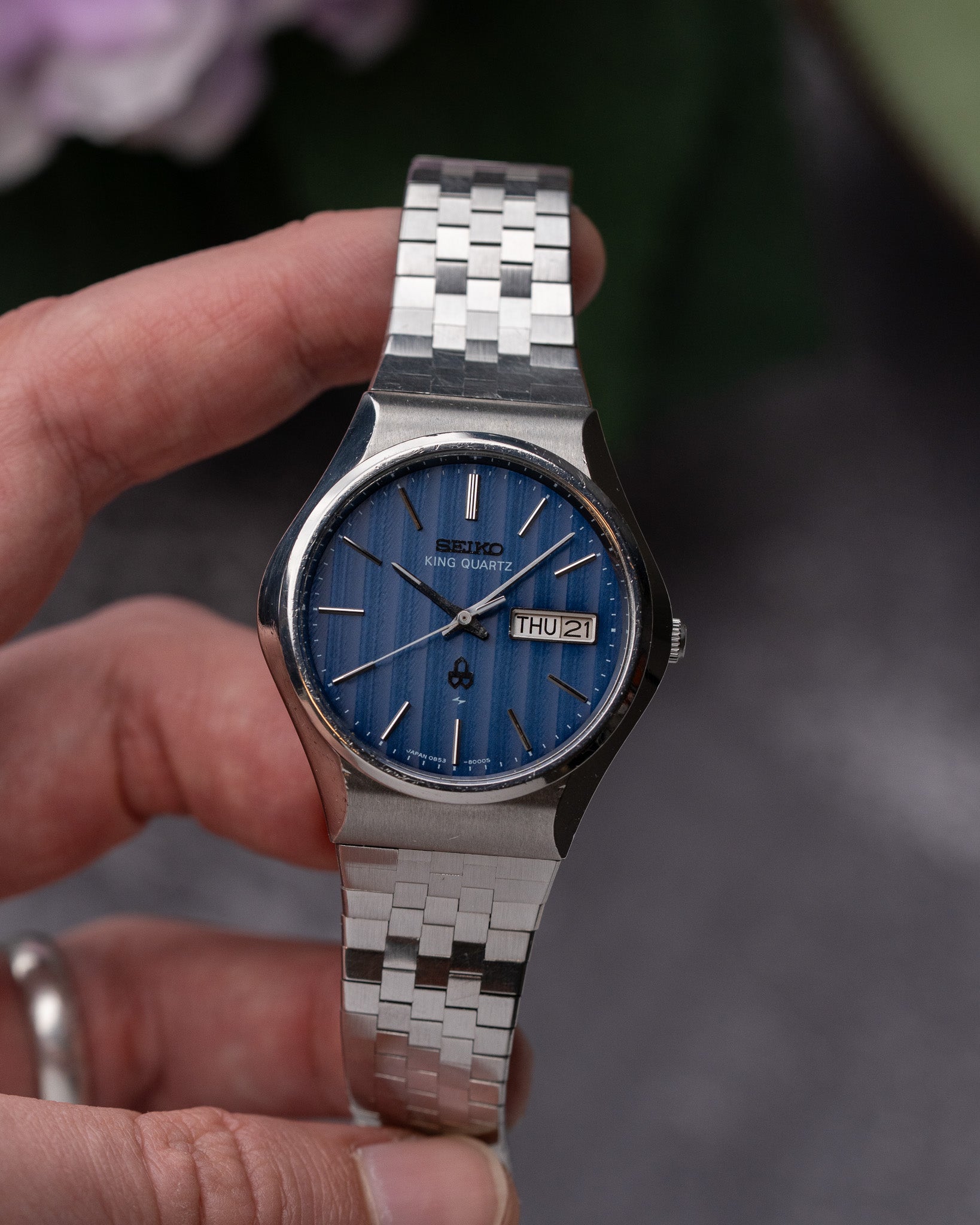 Silver watch with blue face held by a hand against a blurred background