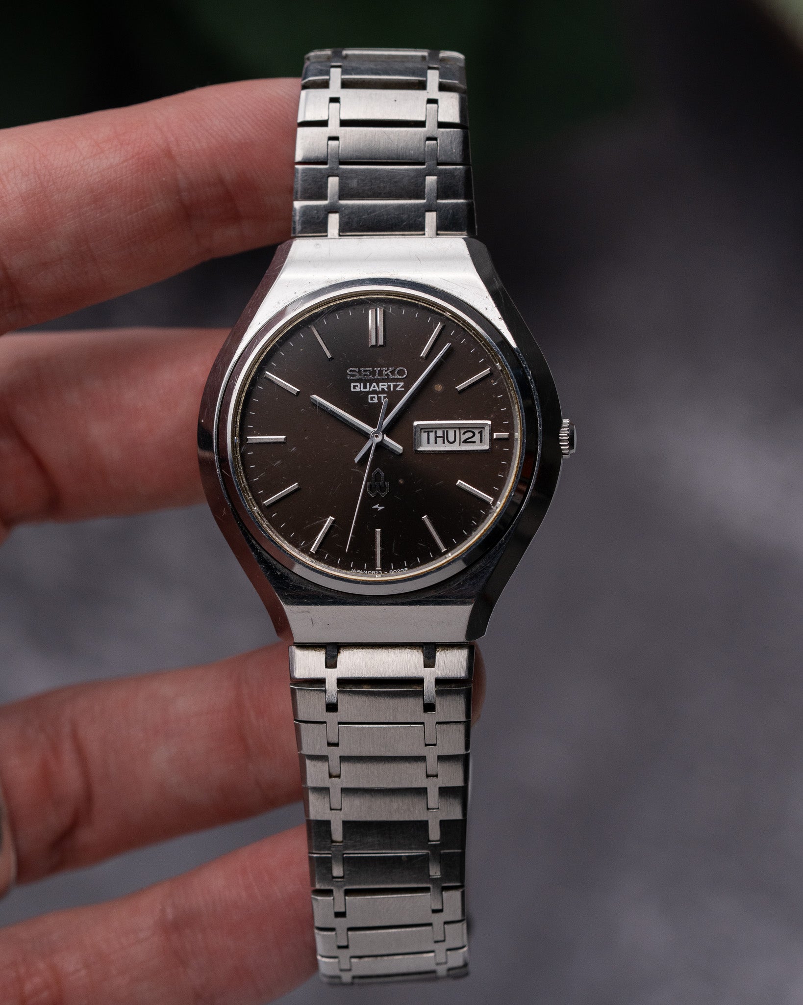 Silver watch with a dark face held by a hand against a blurred background