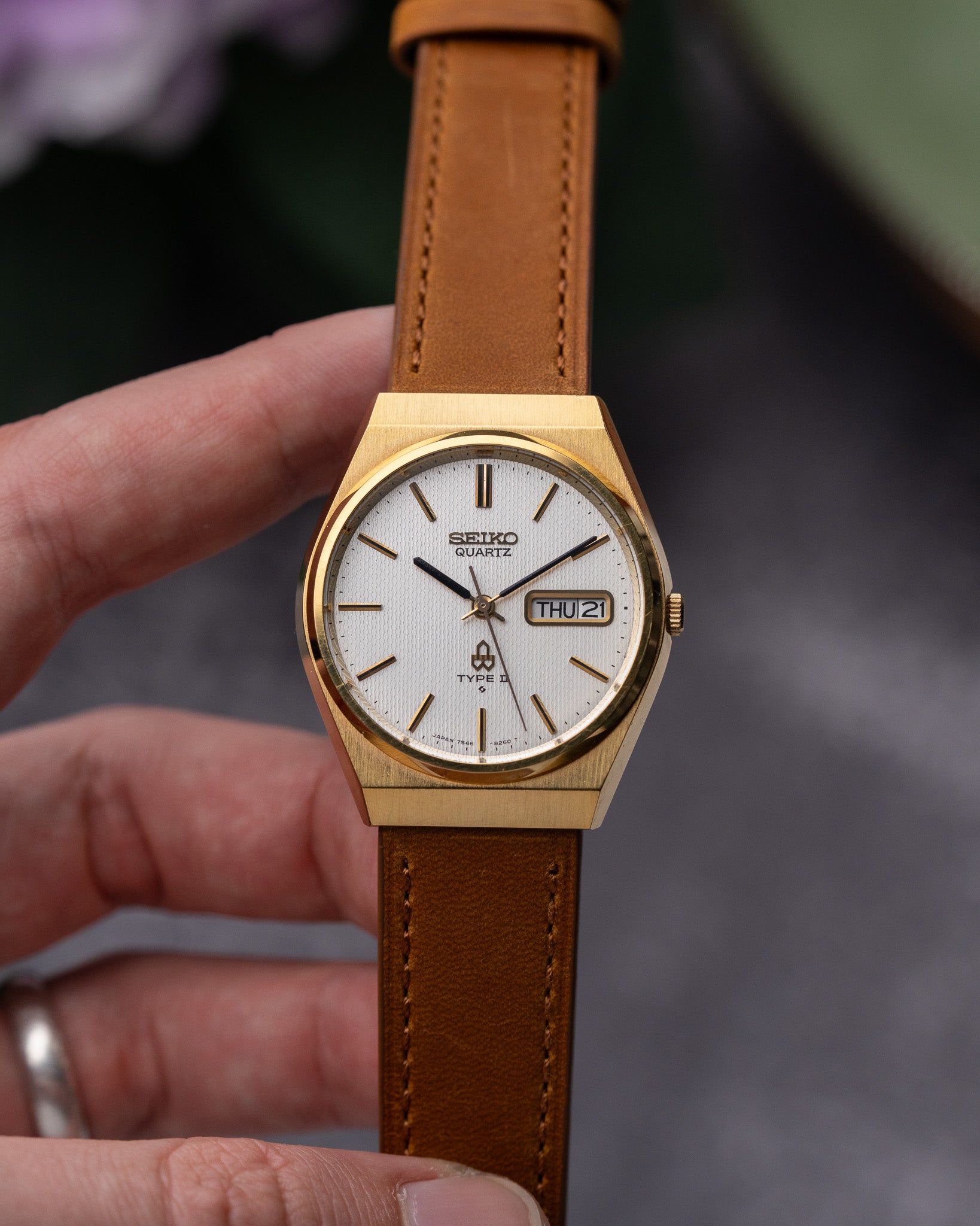 Gold Seiko watch with brown leather strap held by a hand against a blurred background