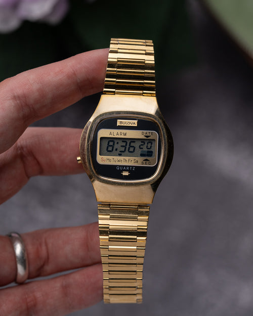 Gold digital watch held by a hand with a blurred background