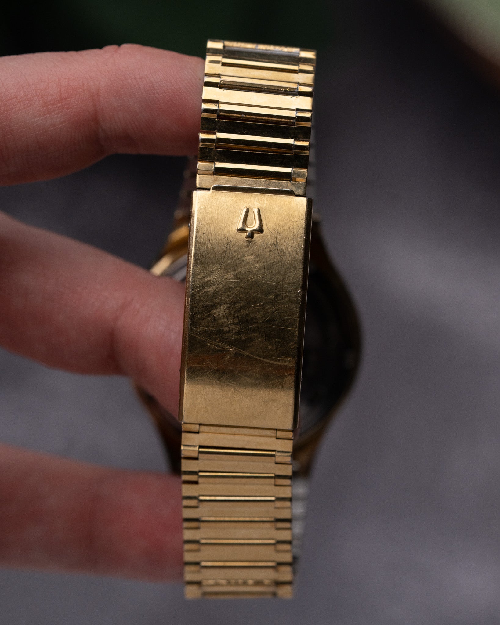 Gold watch band held by a hand against a blurred background