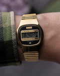 Gold digital watch on a wrist with a plaid sleeve