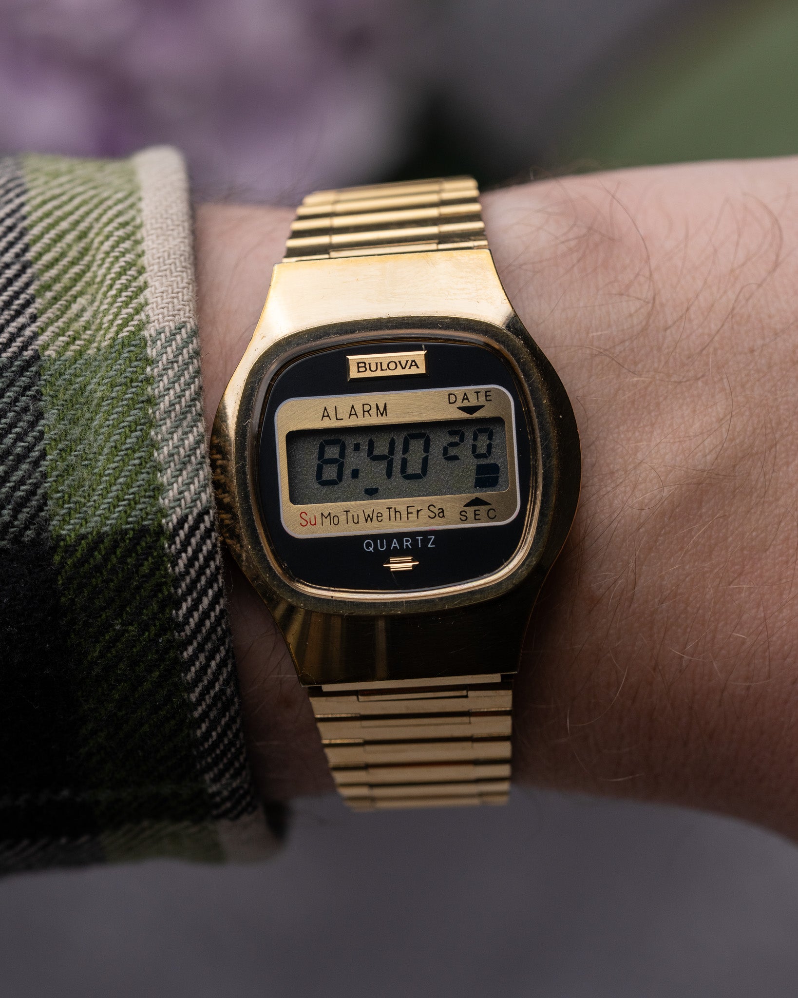 Gold digital watch on a wrist with a plaid sleeve